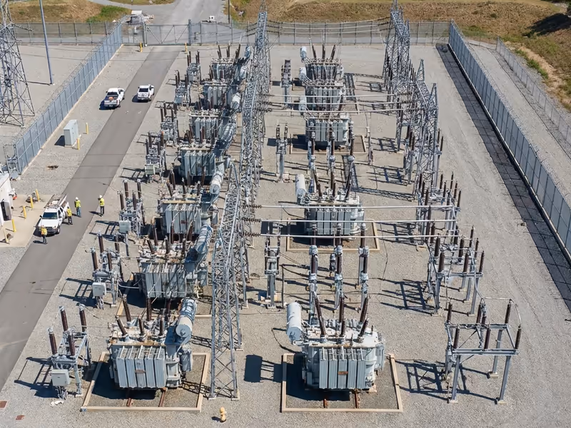 Aerial view of an electrical substation with transformers, power lines, and workers