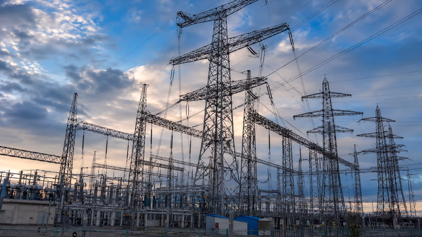 Aerial view of an illuminated electrical substation with high voltage towers at dusk