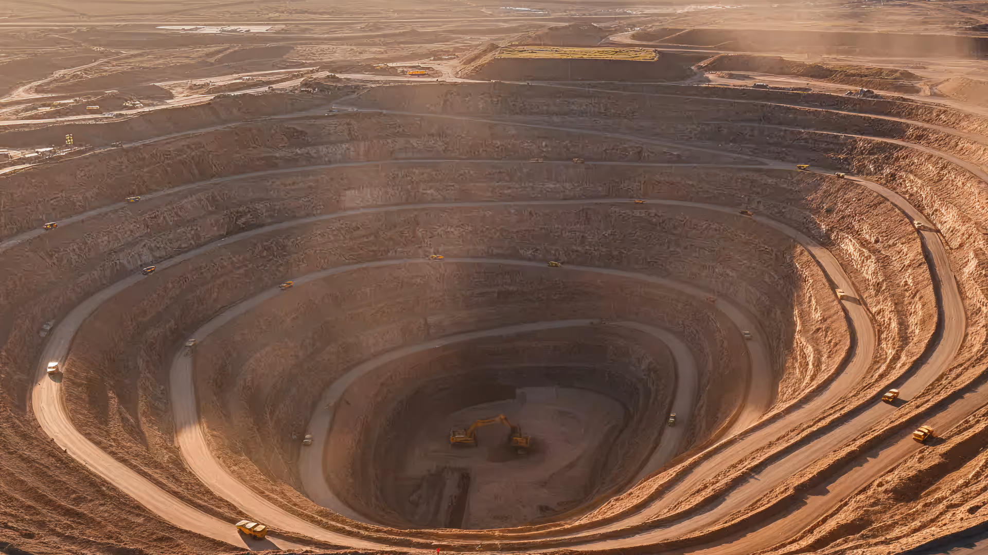 A large open-pit mine with multiple terraced levels and mining trucks driving along the winding road